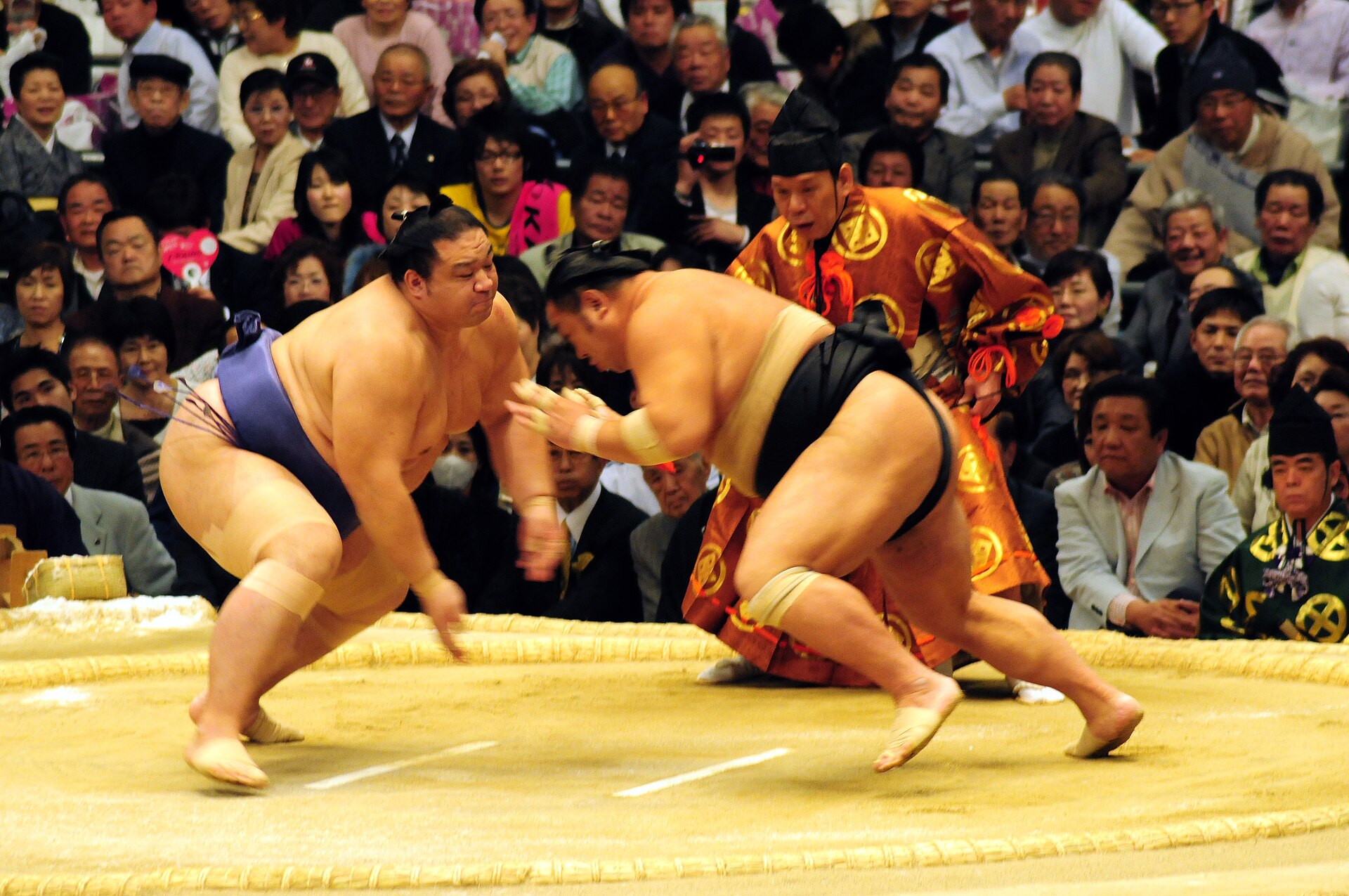 Two wrestlers colliding at the start of a bout as the referee watches.