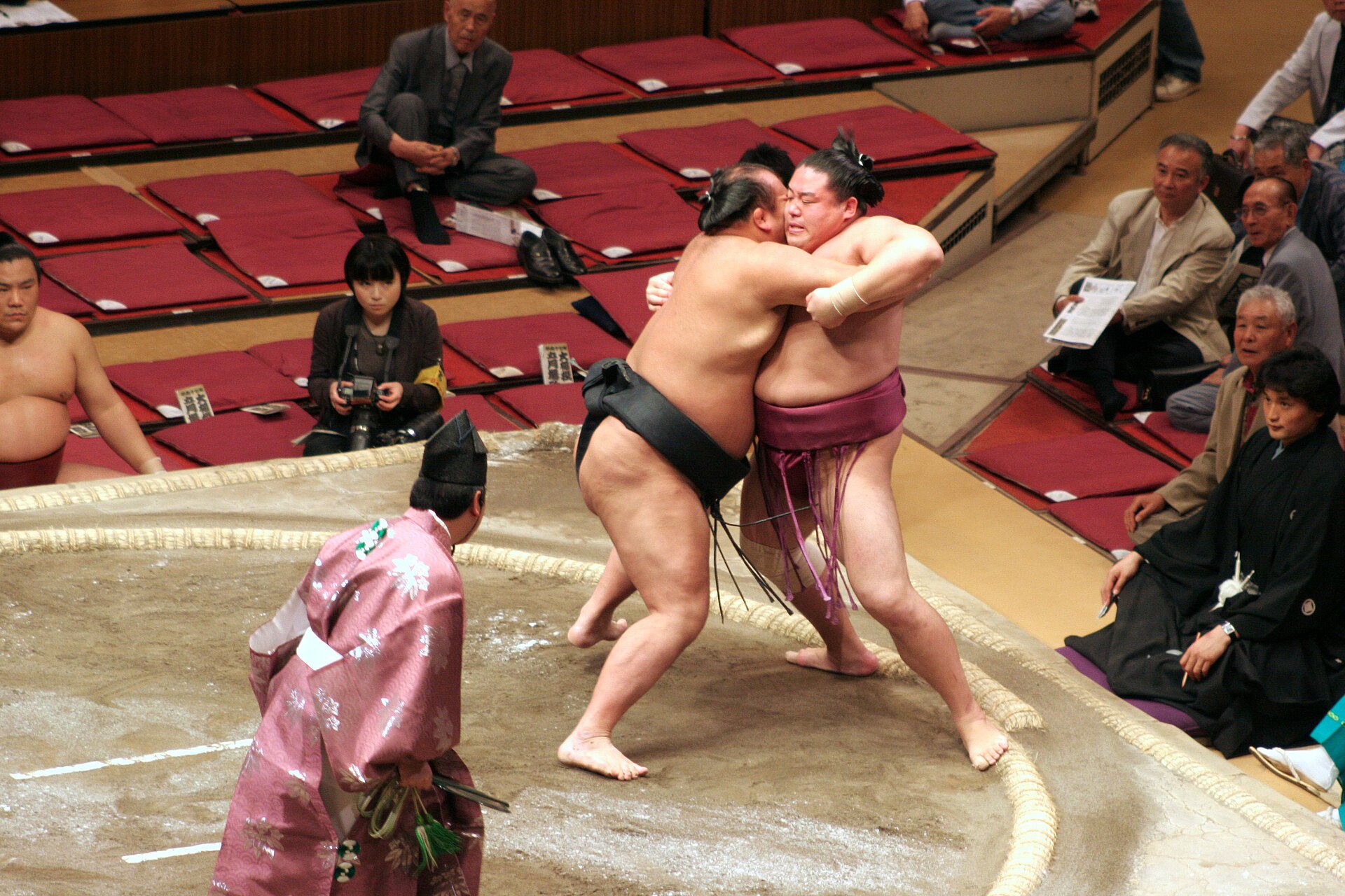 Two wrestlers locked in a belt grip at the edge of the ring.